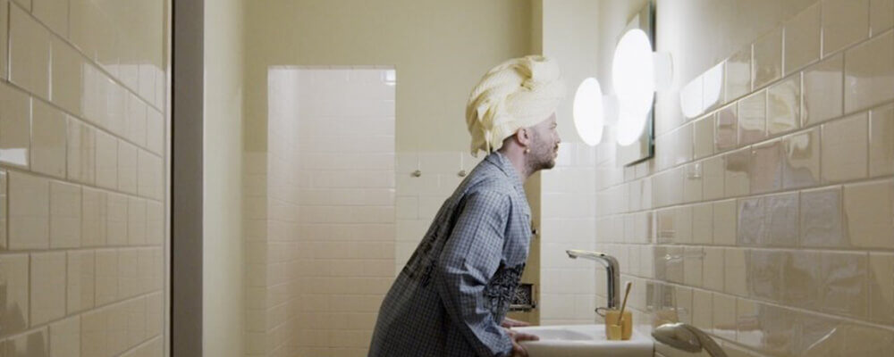 Man met handdoekwikkel op hoofd kijkt in badkamerspiegel