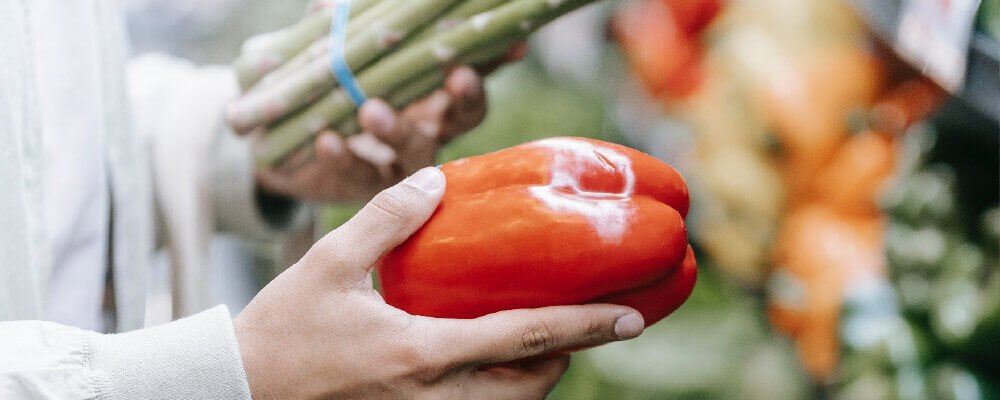 Een rode paprika en een bos asperges worden ieder in een hand vastgehouden
