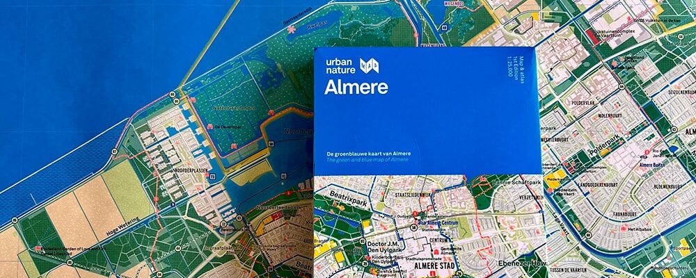 De groen blauwe kaart van Almere ligt ingevouwen op een uitgevouwen groen blauwe kaart van Almere.