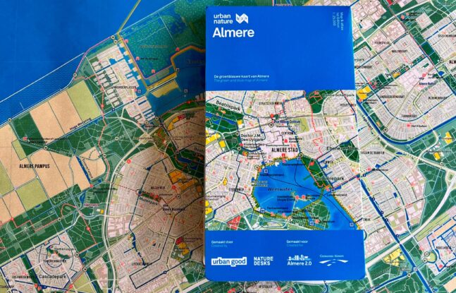 De groen blauwe kaart van Almere ligt ingevouwen op een uitgevouwen groen blauwe kaart van Almere.