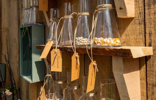 Glazen potten versierd met touw en een label, staan op een houten plank en bevatten verschillende gedroogde erwten, mais en zaden
