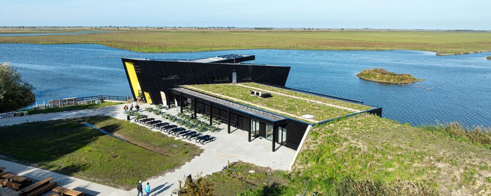 Luchtfoto van het vernieuwde Natuurbelevingcentrum de Oostvaarders in een waterrijke omgeving.