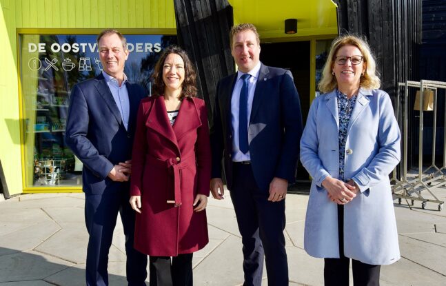 V.l.n.r.: directeur Boudewijn Revis, wethouder Maaike Veeningen, gedeputeerde Harold Hofstra en directeur-bestuurder van Stad & Natuur Liesbeth Bronkhorst voor de ingang van De Oostvaarders met gele muur op de achtergrond.