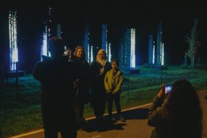 Een familie poseert voor lichtgevende kunstinstallaties in de buitenlucht, waarbij iemand hen fotografeert in het donker.