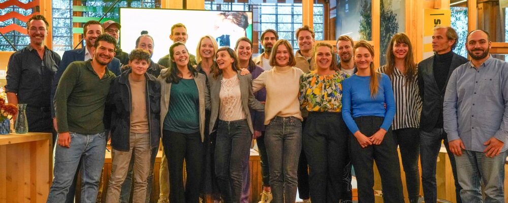 Groepsfoto van deelnemers en organisatoren van het Food Pioneers-programma bij Flevo Campus, lachend en samen voor een scherm in een houten conferentieruimte - Foto: Nicolas Brenninkmeijer